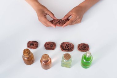 top view of partial fortune teller holding clay rune near jars with essential oils clipart