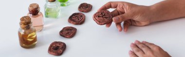 cropped view of predictor holding clay rune near bottles with essential oils, banner