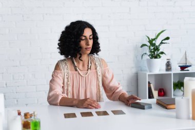 young fortune teller sitting near deck of tarot cards and prediction book