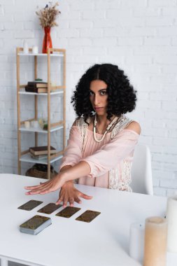 KYIV, UKRAINE - JUNE 29, 2022: young oracle looking at camera while predicting on tarot cards