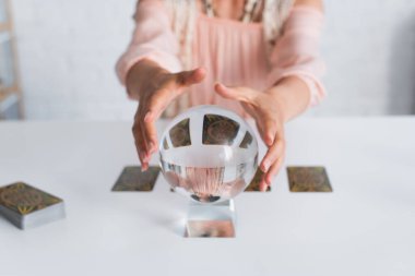 KYIV, UKRAINE - JUNE 29, 2022: selective focus of crystal ball near cropped fortune teller on blurred background