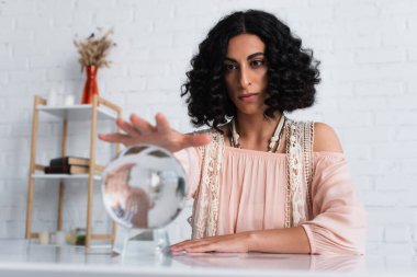 brunette fortune teller holding hand over crystal ball during spiritual session