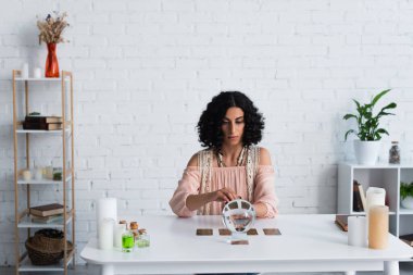 brunette astrologist near magic sphere and tarot cards during spiritual session at home