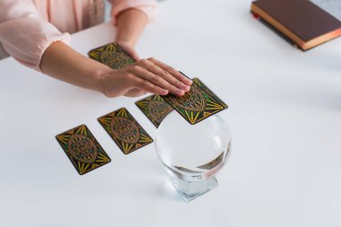 KYIV, UKRAINE - JUNE 29, 2022: high angle view of cropped predictor holding tarot card near magic orb at home