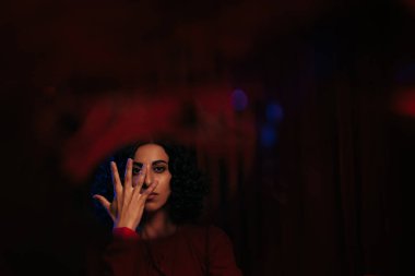 portrait of brunette soothsayer obscuring face with hand and looking at camera on dark background