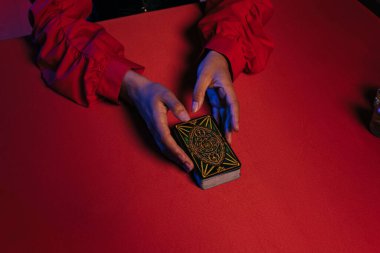 KYIV, UKRAINE - JUNE 29, 2022: high angle view of cropped medium holding tarot cards near red table