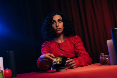 KYIV, UKRAINE - JUNE 29, 2022: young fortune teller holding tarot cards during spiritual session on dark background