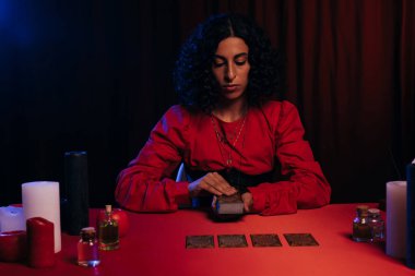 KYIV, UKRAINE - JUNE 29, 2022: young woman predicting future on tarot cards on red table and dark background