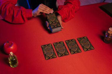 KYIV, UKRAINE - JUNE 29, 2022: partial view of oracle laying out tarot cards on red table near essential oils