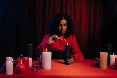 young oracle lighting palo santo stick near burning candles on dark background