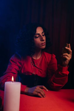fortune teller looking at bottle with essential oil near burning candle on dark background