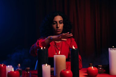 medium holding hand over burning candles during spiritual session in darkness