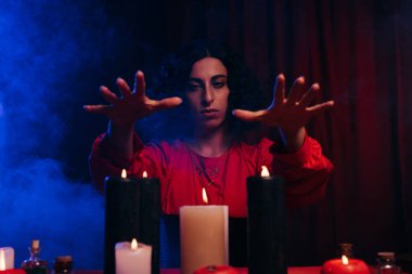 medium holding hands above burning candles near blue smoke on dark background