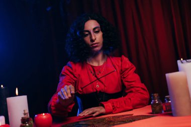 young fortune teller holding palo santo stick near tarot cards on dark background