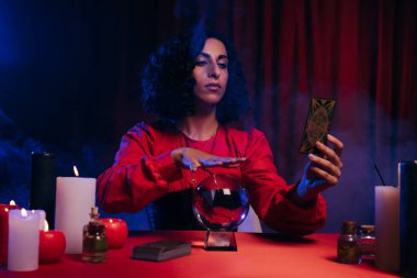 KYIV, UKRAINE - JUNE 29, 2022: fortune teller with tarot card holding hand over crystal ball during spiritual session