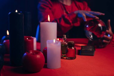 selective focus of blurred candles near cropped fortune teller and crystal ball isolated on black
