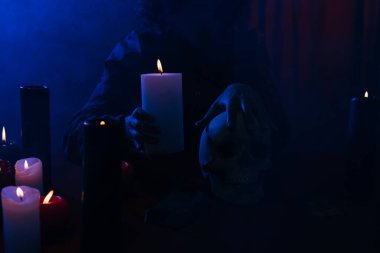 cropped view of oracle with burning candle and skull during magic session in darkness near blue smoke