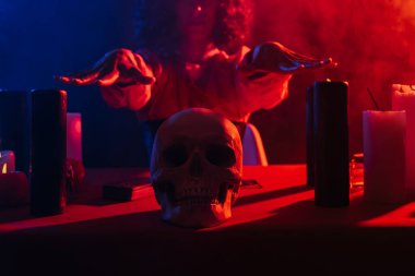 cropped view of blurred medium near skull and candles on dark background with colorful smoke