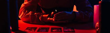 KYIV, UKRAINE - JUNE 29, 2022: partial view of future predictor with burning candle near tarot cards isolated on black, banner