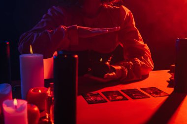 KYIV, UKRAINE - JUNE 29, 2022: cropped view of fortune teller holding burning candle during spiritual session in darkness