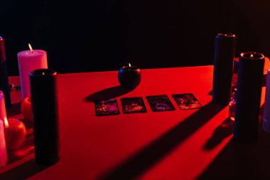 KYIV, UKRAINE - JUNE 29, 2022: tarot cards and burning candles on red table isolated on black