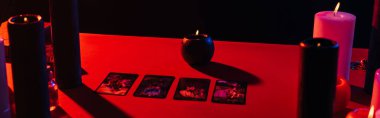 KYIV, UKRAINE - JUNE 29, 2022: red table with candles and tarot cards isolated on black, banner