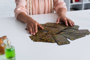 KYIV, UKRAINE - JUNE 29, 2022: cropped view of predictor near tarot cards and blurred bottles with essential oils