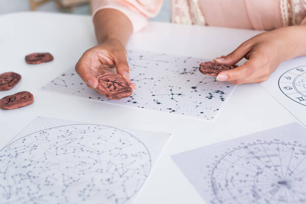 partial view of young astrologer holding clay runes near cosmic maps at home