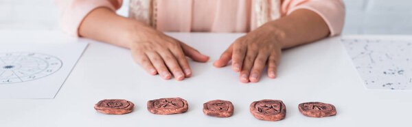 partial view of fortune teller sitting near clay runes and star charts, banner