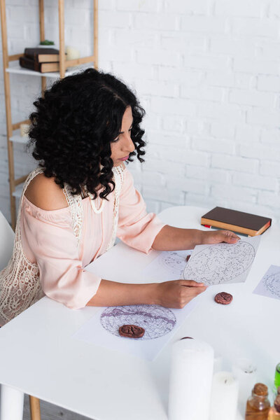 brunette astrologer looking at star charts near clay runes and prediction book