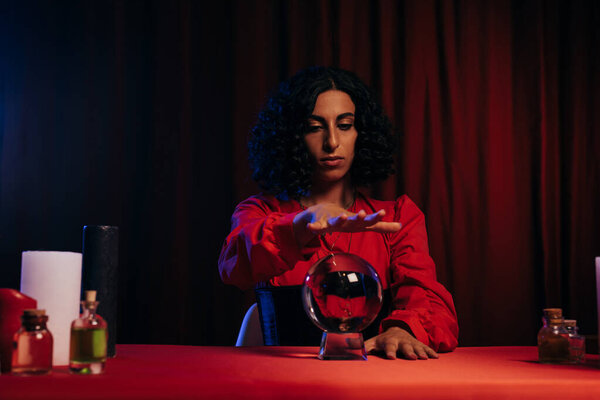 brunette oracle near crystal ball and essential oils on dark background