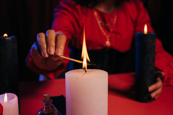 cropped view of blurred fortune teller lighting palo santo stick near burning candle isolated on black