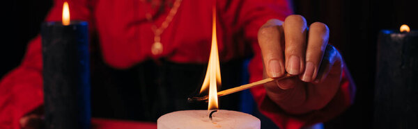 partial view of fortune teller lighting palo santo stick near burning candle isolated on black, banner