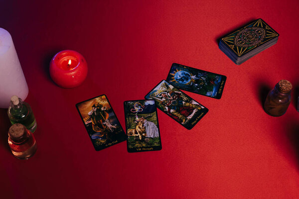 KYIV, UKRAINE - JUNE 29, 2022: top view of tarot cads near burning candles and essential oils on red table
