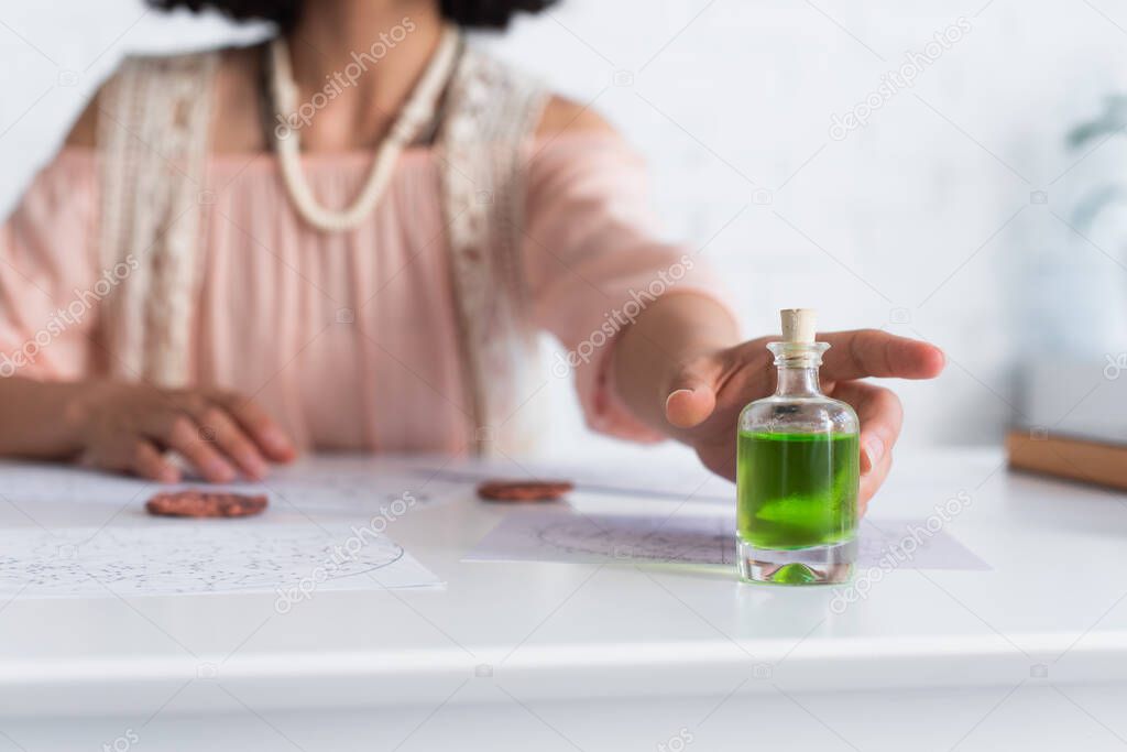 selective focus of bottle with essential oil near cropped astrologer and clay runes