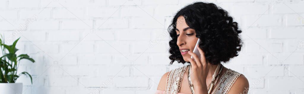 smiling brunette fortune teller talking on mobile phone at home, banner