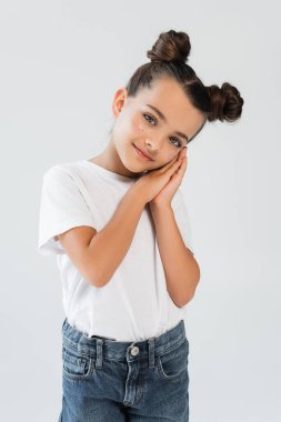 smiling girl with folded hands and glitter stars on cheeks posing isolated on grey
