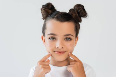 portrait of cheerful girl with lip gloss and sparkling glitter stars pointing at face isolated on grey