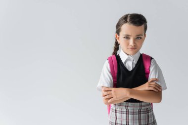 sad schoolgirl with backpack standing with crossed arms isolated on grey