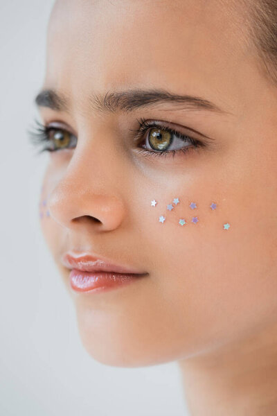 close up view of adorable girl with lip gloss and sparkling glitter stars on face isolated on grey