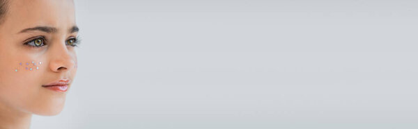 close up view of adorable girl with lip gloss and sparkling glitter stars on face isolated on grey, banner