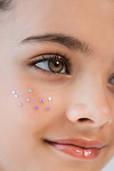 close up view of happy girl with sparkling glitter on cheek looking away