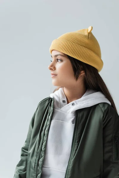 cute girl in yellow beanie hat and bomber jacket looking away isolated on grey