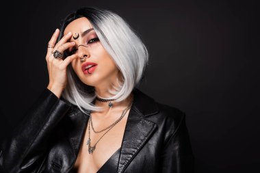 Kül sarısı saçlı ve cadı makyajlı seksi kadın yüzünü gizliyor ve siyah kameraya bakıyor.