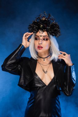 Siyah çelenk ve deri ceketli seksi cadı stili kadın. Arka planda mavi bir sis var.