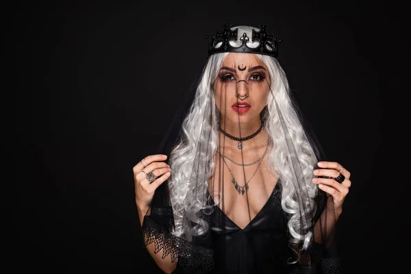 blonde witch style woman in crown and veil looking at camera isolated on black