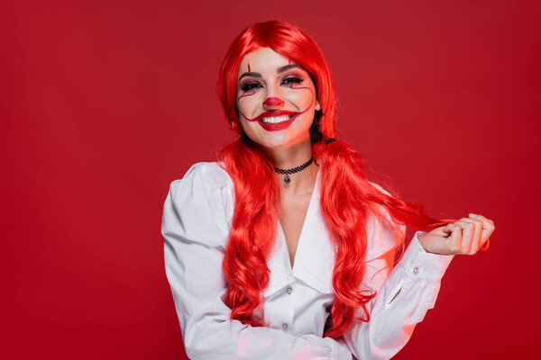 joyful woman with clown halloween makeup and bright hair isolated on red