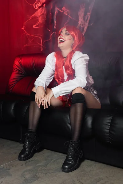 性感的红头发女人 穿着吊袜带的服装 在深色背景的皮沙发上 用蜘蛛网笑着 — 图库照片