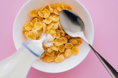 Şişeden kaseye, mısır gevreği ve pembe kaşıkla akan sütün üst görüntüsü. 