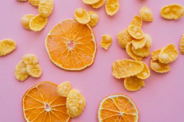 top view of dried oranges near corn flakes on pink background clipart